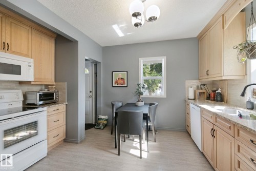 Kitchen featuring light wood-finish cabinetry, light stone-finish countertops, tile backsplash, and light wood-finish flooring - 12035 83 Street Nw, Edmonton, AB 