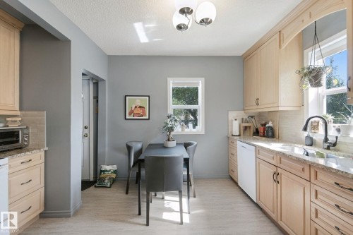 Light-toned kitchen cabinetry with dark hardware, granite countertops, tile backsplash, and a contemporary ceiling fixture - 12035 83 Street Nw, Edmonton, AB 