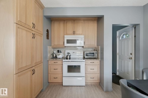 Wood-finish flooring, light wood cabinetry, white subway tile backsplash, light-toned countertops, and an integrated oven range - 12035 83 Street Nw, Edmonton, AB 
