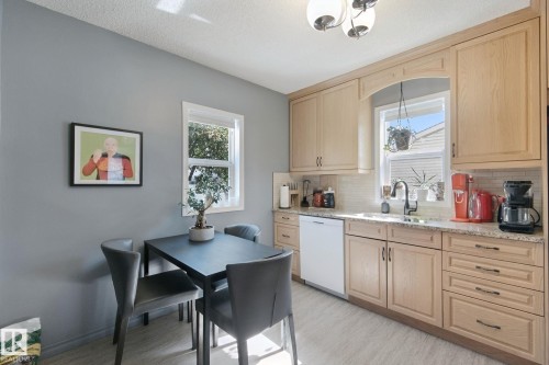 Bright kitchen featuring natural wood cabinetry with ample storage, white subway tile backsplash, stainless steel sink with chrome faucet, and integrated appliances - 12035 83 Street Nw, Edmonton, AB 