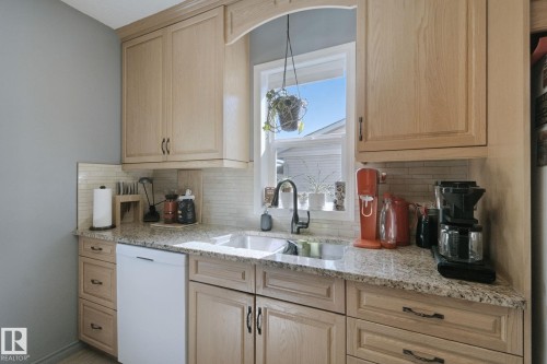 Light wood-finish cabinetry, granite countertops, tile backsplash, stainless steel double basin sink, and black pull-down faucet - 12035 83 Street Nw, Edmonton, AB 