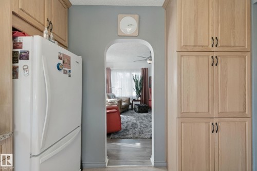 Wood-finish cabinetry with dark hardware, white refrigerator, and an arched entryway - 12035 83 Street Nw, Edmonton, AB 