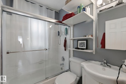 Bathtub with sliding glass shower doors, wall-mounted shelving, pedestal sink, and mounted mirror - 12035 83 Street Nw, Edmonton, AB 