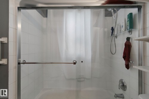 Bathtub with glass sliding doors, chrome hardware, white tile surround, and a wall-mounted showerhead - 12035 83 Street Nw, Edmonton, AB 