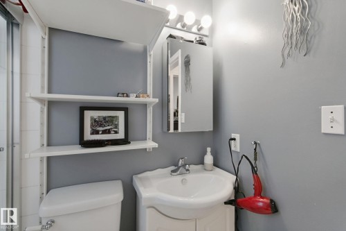 Wall-mounted shelving units, an attached vanity with an integrated sink, a wall-mounted medicine cabinet with a mirrored door, a chrome-finish faucet, and a four-bulb vanity light fixture - 12035 83 Street Nw, Edmonton, AB 