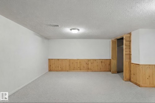 Finished basement featuring neutral carpeting, wood-paneled wainscoting, recessed ceiling lighting, and a closet with louvered wooden doors.  This photo has been virtually decluttered and white wall has wainscoting. - 12035 83 Street Nw, Edmonton, AB 