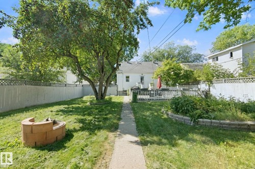 Expansive backyard featuring a mature tree, paved pathway, raised garden bed, and a brick fire pit - 12035 83 Street Nw, Edmonton, AB 