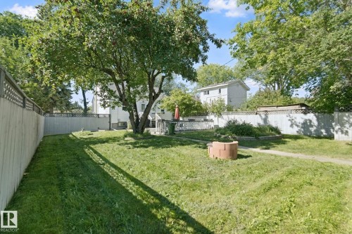 Expansive backyard featuring a mature tree, perimeter fencing, brick fire pit, and a raised garden bed - 12035 83 Street Nw, Edmonton, AB 