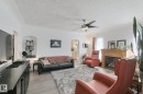 Living area featuring light wood-finish flooring, a built-in fireplace with a wood mantle, a ceiling fan with integrated lighting, and an arched entryway - 12035 83 Street Nw, Edmonton, AB 