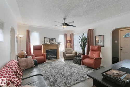 Living area featuring a gas fireplace with wood mantel, ceiling fan with light fixture, light wood-finish flooring, and arched doorways - 12035 83 Street Nw, Edmonton, AB 