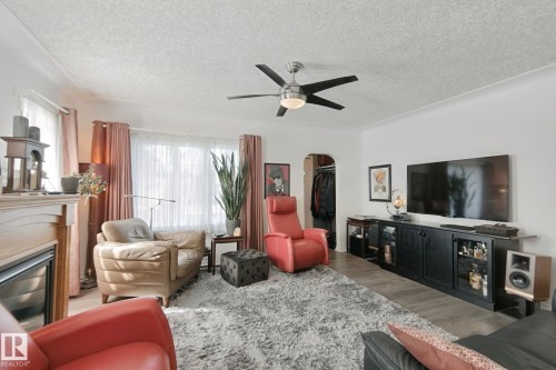 Living area with wood-finish flooring, a ceiling fan with integrated lighting, and a fireplace featuring a light-toned mantel - 12035 83 Street Nw, Edmonton, AB 