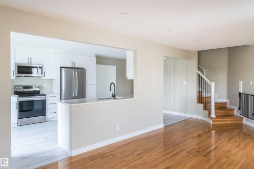 Open-concept kitchen featuring white cabinetry, stainless steel appliances, and a breakfast bar - 5010 147 Street Nw, Edmonton, AB 