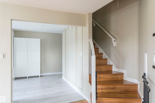 Entryway featuring a wood staircase with white risers and a white handrail, complemented by a black metal baluster - 5010 147 Street Nw, Edmonton, AB 