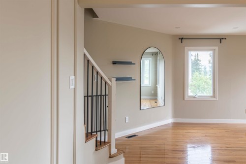 Hardwood-finish flooring extending into living spaces, staircase with black metal balusters, and a window with white trim - 5010 147 Street Nw, Edmonton, AB 