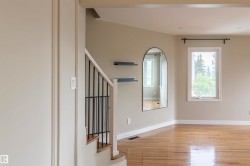 Hardwood-finish flooring extending into living spaces, staircase with black metal balusters, and a window with white trim - 