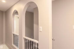 Hallway featuring arched doorways, recessed lighting, white balusters with black spindles, and light-toned wall paint - 