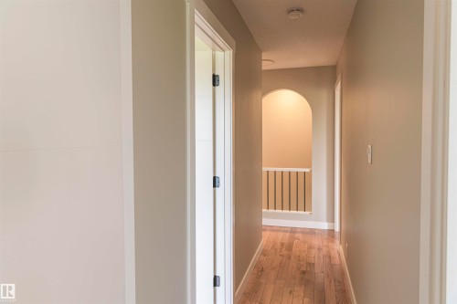 Hallway featuring wood-finish flooring, neutral wall paint, white trim, an arched entryway, and a white balustrade - 5010 147 Street Nw, Edmonton, AB 