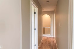Hallway featuring wood-finish flooring, neutral wall paint, white trim, an arched entryway, and a white balustrade - 