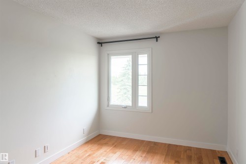 White-painted room featuring a multi-pane window with white trim, a black curtain rod, and wood-finish flooring - 5010 147 Street Nw, Edmonton, AB 