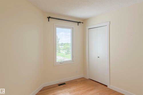 Bedroom featuring a window with exterior views, light-toned walls, wood-finish flooring, a bi-fold closet, and white trim - 5010 147 Street Nw, Edmonton, AB 