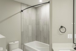 Bathtub and shower combination featuring large format grey tile surround and a curved matte black shower rod - 