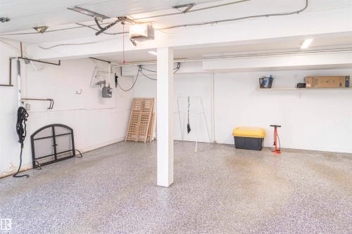 Spacious garage featuring a durable speckled epoxy floor, overhead lighting, an exposed beam ceiling, and a built-in wall shelf - 5010 147 Street Nw, Edmonton, AB 