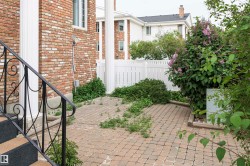 Brick exterior featuring white architectural columns, black wrought iron railings, and a paver stone patio - 