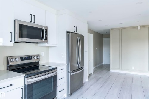 Modern kitchen featuring white cabinetry with matte black hardware, stainless steel appliances, light-toned countertops, and light wood-finish flooring - 5010 147 Street Nw, Edmonton, AB 