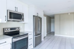 Modern kitchen featuring white cabinetry with matte black hardware, stainless steel appliances, light-toned countertops, and light wood-finish flooring - 