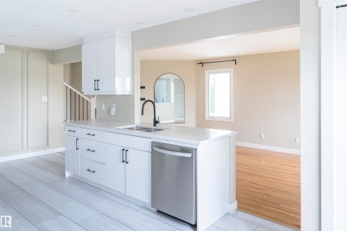 Modern kitchen island featuring white cabinetry, a single basin sink with a matte black faucet, and a stainless steel dishwasher - 5010 147 Street Nw, Edmonton, AB 