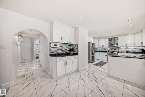 Kitchen featuring glossy white cabinetry, black countertops, and a mosaic tile backsplash - 4608 43 Avenue Nw, Edmonton, AB 