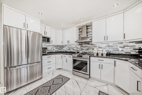 Modern kitchen featuring white cabinetry, stainless steel appliances, dark countertops, a tiled backsplash, and recessed lighting - 4608 43 Avenue Nw, Edmonton, AB 