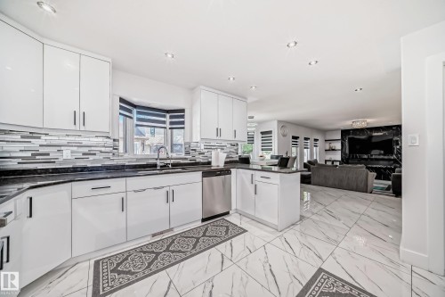 Gourmet kitchen featuring sleek white cabinetry, dark countertops, a mosaic tile backsplash, and stainless steel appliances - 4608 43 Avenue Nw, Edmonton, AB 
