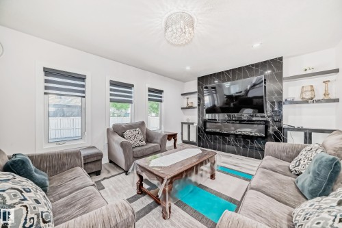 White walls with recessed lighting, chandelier lighting fixture, black accent wall with built-in fireplace, three windows with roller shades, and light wood-finish flooring - 4608 43 Avenue Nw, Edmonton, AB 
