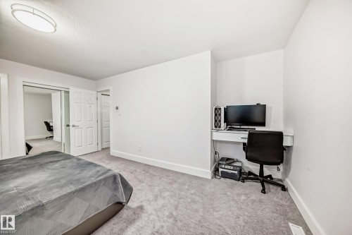 Carpeted room featuring a built-in desk, overhead flush-mount lighting, and white paneled doors - 4608 43 Avenue Nw, Edmonton, AB 