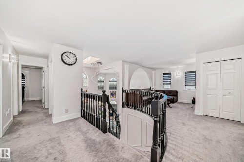 Curved dark wood staircase railing, light gray carpeting, white bi-fold closet doors, wall sconce lighting, and arched doorway - 4608 43 Avenue Nw, Edmonton, AB 