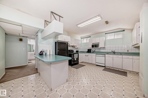 Kitchen featuring a peninsula with countertop, white cabinetry, integrated appliances, and a tiled backsplash - 4608 43 Avenue Nw, Edmonton, AB 