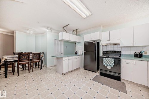 Kitchen featuring white cabinetry, black appliances, light-colored countertops, and patterned flooring - 4608 43 Avenue Nw, Edmonton, AB 