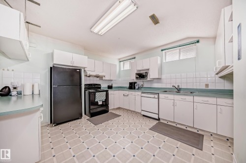 Kitchen featuring white cabinetry, a black refrigerator, a black range, a white dishwasher, and light blue countertops - 4608 43 Avenue Nw, Edmonton, AB 