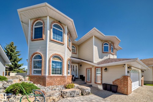 Property exterior featuring architectural brick accents, multiple arched windows, siding, a paver stone walkway, and an attached garage with a white door - 4608 43 Avenue Nw, Edmonton, AB 