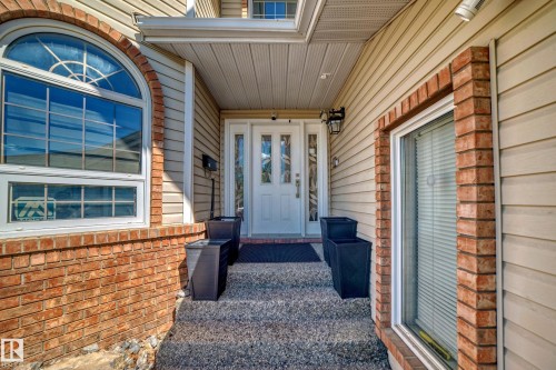 Entryway featuring a white door with decorative glass inserts, an arched window with grilles, brick accents, and light-toned siding - 4608 43 Avenue Nw, Edmonton, AB 