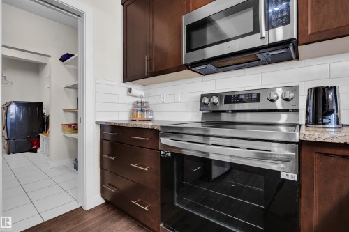 Kitchen area featuring rich wood-finish cabinetry with stainless steel appliances, granite-style countertops, and a subway tile backsplash - 3071 Carpenter Landing Sw, Edmonton, AB 