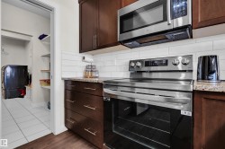 Kitchen area featuring rich wood-finish cabinetry with stainless steel appliances, granite-style countertops, and a subway tile backsplash - 