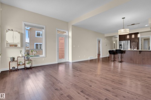 Spacious living area featuring wide plank wood-finish flooring, light neutral wall tones, and abundant natural light from a large window - 3071 Carpenter Landing Sw, Edmonton, AB 