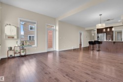 Spacious living area featuring wide plank wood-finish flooring, light neutral wall tones, and abundant natural light from a large window - 