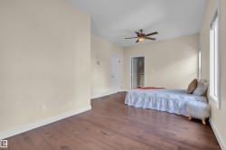 Spacious interior room featuring wood-finish flooring, light-toned walls, and a ceiling fan - 