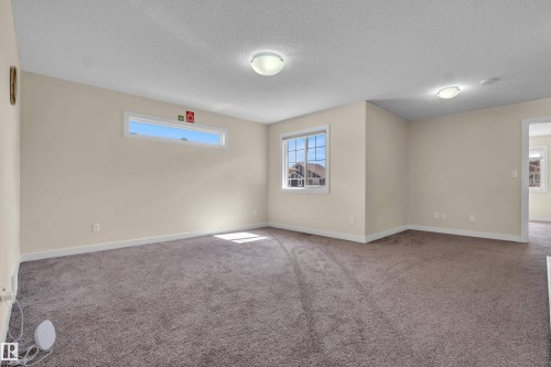 Spacious room featuring neutral carpeting, light beige walls, multiple windows, and flush-mount ceiling lighting - 3071 Carpenter Landing Sw, Edmonton, AB 