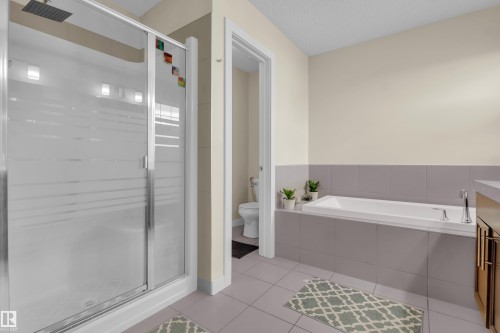 Spacious bathroom featuring a glass-enclosed shower with rainfall showerhead, a large soaking tub, and neutral tiled flooring - 3071 Carpenter Landing Sw, Edmonton, AB 