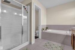 Spacious bathroom featuring a glass-enclosed shower with rainfall showerhead, a large soaking tub, and neutral tiled flooring - 