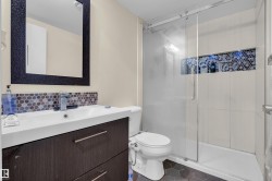 Contemporary bathroom featuring a dark wood-finish vanity with an integrated white sink, a mosaic tile backsplash, a frameless mirror with a textured black frame, a glass-enclosed shower with subway tile surround, and hexagonal floor tiles - 